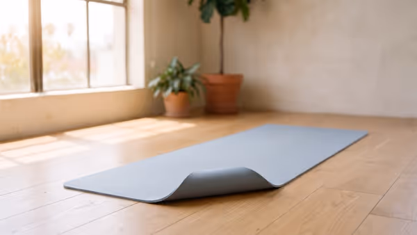 A plain blue-grey yoga mat lying flat on a light oak floor with one corner turned up — an illustration of the mat type, not a photograph of a Target All in Motion mat