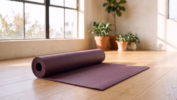 A plain plum-purple natural rubber yoga mat, matte and slightly grainy, partly rolled on a light oak floor — an illustration of the mat type, not a photograph of a Jade mat