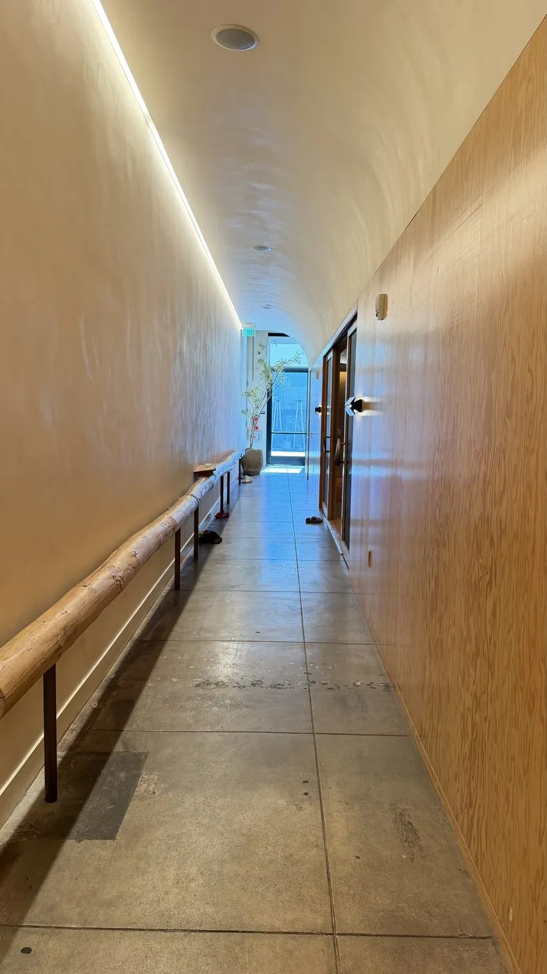 A long, narrow corridor with a curved white ceiling washed by a strip of light, a wooden handrail along one wall and plywood panelling along the other