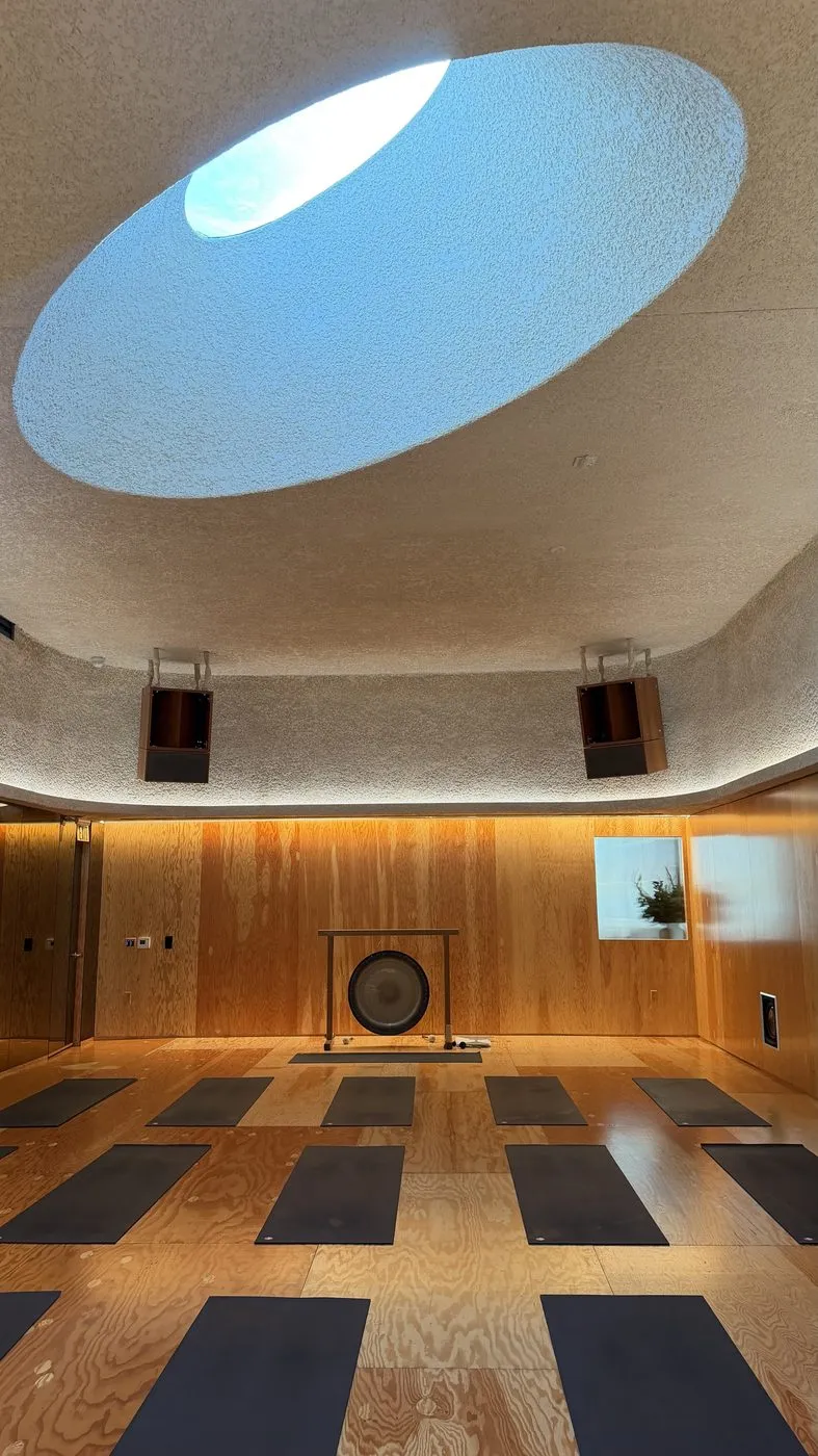 Looking up at the oval skylight cut into the textured ceiling, above rows of mats and the gong at the front of the room