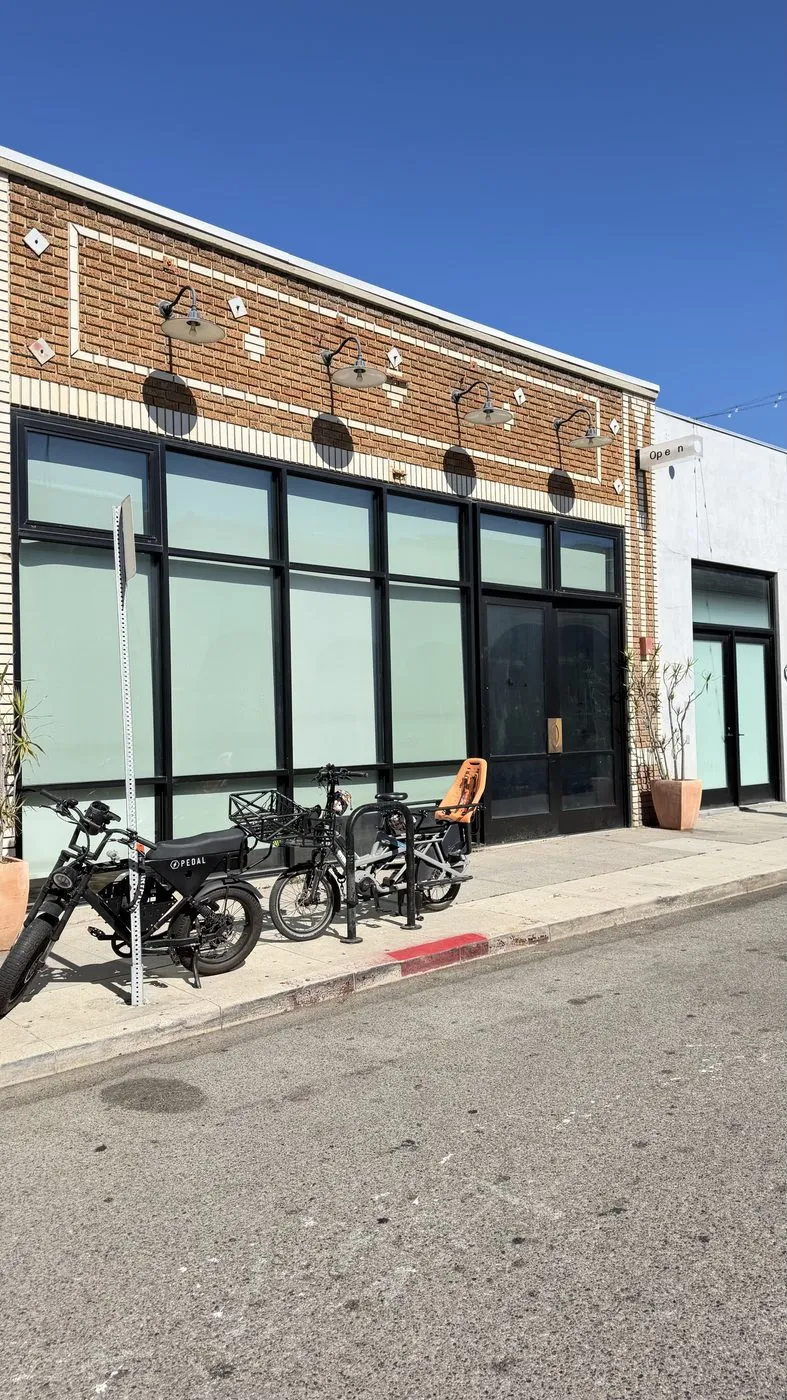 The building on Market Street, a brick facade with black-framed frosted windows and four gooseneck lamps, bikes parked at the curb, and a small blade sign reading Open at the corner