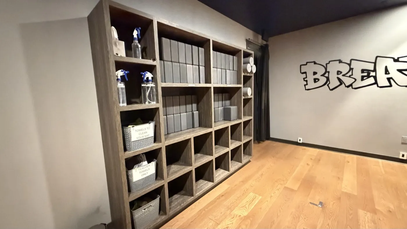 Prop shelving in a studio room: wooden cubbies holding stacked blocks, folded blankets and spray bottles, with the graffiti wall lettering beyond.