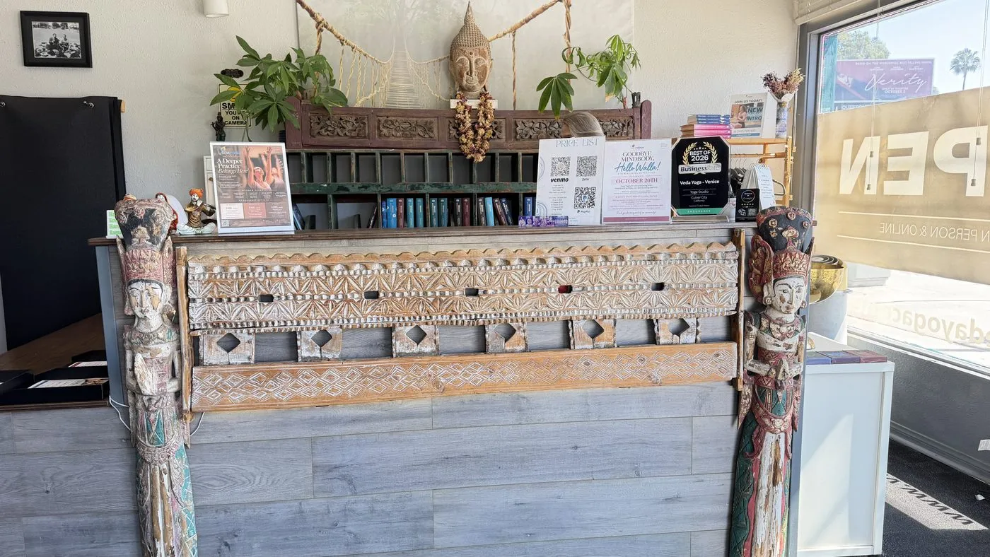 The reception desk, a long counter fronted with a carved and white-painted antique panel between two carved pillars, a Buddha head and plants on the shelf above