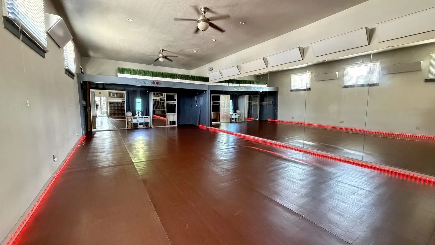 The second practice room, a dark polished wood floor with a mirrored wall along one side, a red light strip at its base and ceiling fans overhead