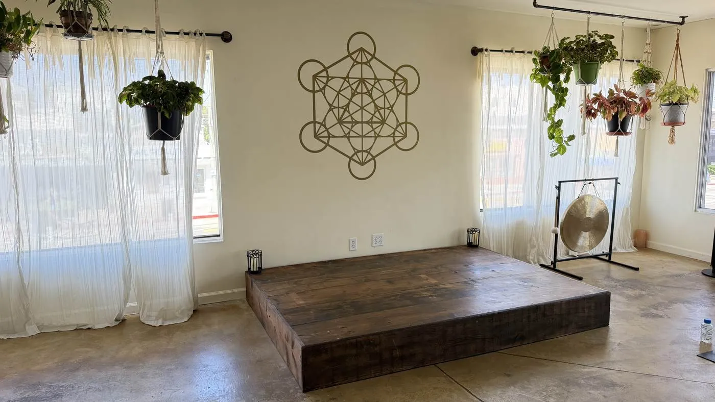 The low wooden platform at the front of the room, a large brass gong on a stand beside it and hanging plants at the curtained windows