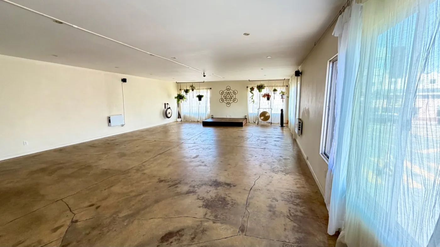 The same room from the opposite end, the platform and gong small beneath the Metatron's Cube decal, with a wall of sheer-curtained windows running down the right